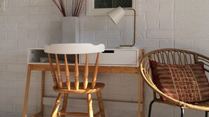 Un espace de travail comprenant une chaise en bois, un bureau blanc et une chaise en osier avec un coussin.
