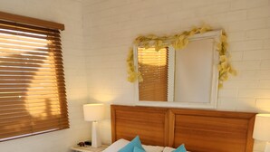 Un lit bien fait, avec une literie blanche et des oreillers bleus et jaunes, une tête de lit en bois et une table de chevet avec une lampe.