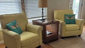 A living room with two yellow armchairs, a glass-top coffee table, and a wooden floor.