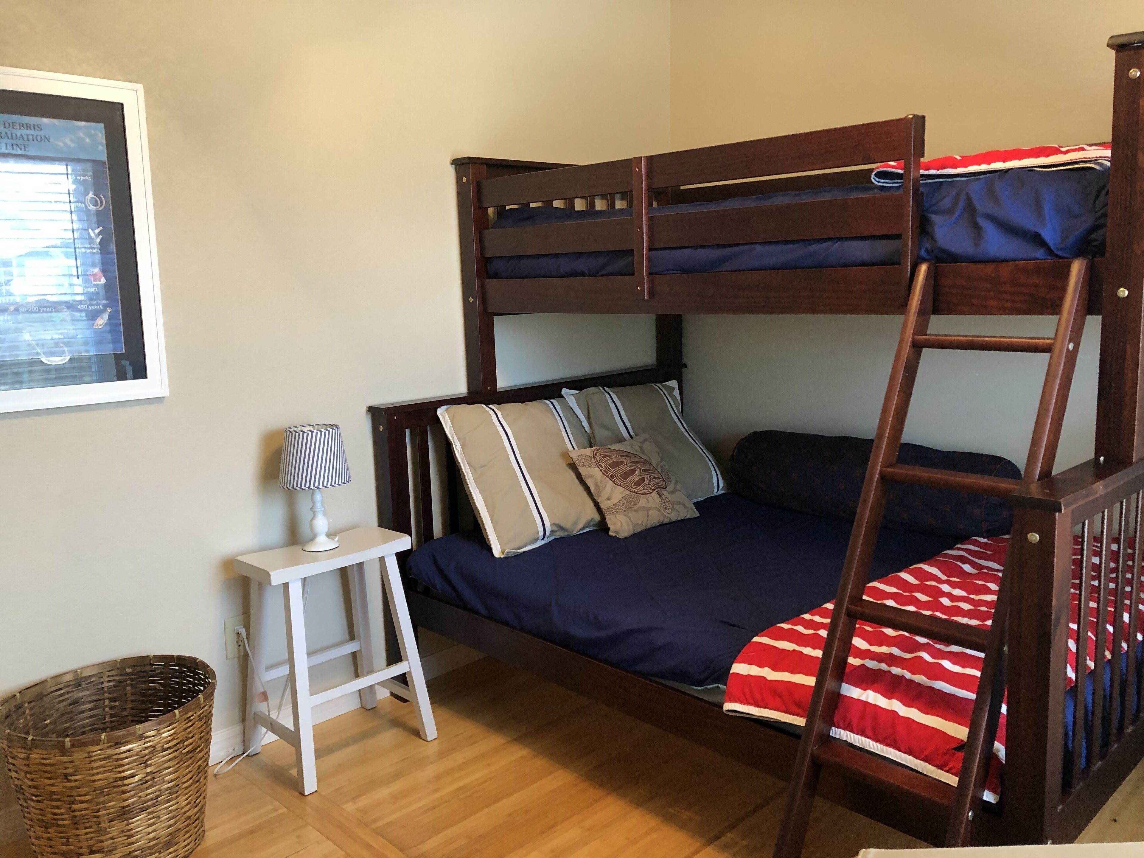 A bunk bed with a ladder, a small white table with a lamp, and a wicker basket.