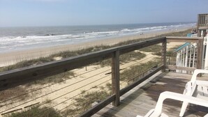 A wooden deck with white plastic chairs overlooking a beach with waves.