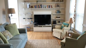 A living room with a flat-screen TV, a ceiling fan, and a bookshelf.