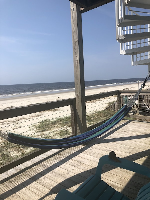 A wooden deck with a hammock and a view of the beach.