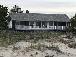 A beachfront house with a covered porch and a sandy beach in the foreground.