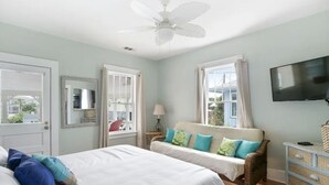 A bedroom with two beds, a ceiling fan, a TV, and a wicker chair. - Cool Ocean View with Balcony! King Bed, Free Parking & Free Wifi! (Tybee Island)