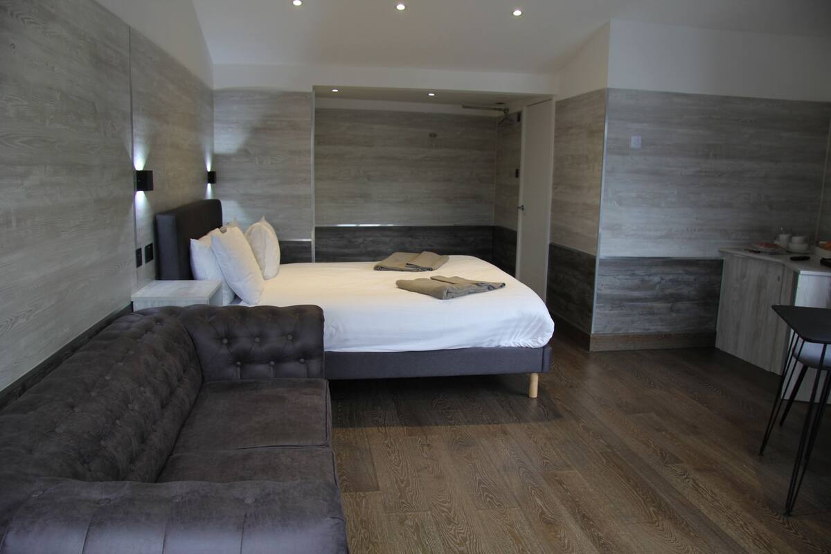 A modern bedroom with a large bed, a dark sofa, and a small table with a chair.