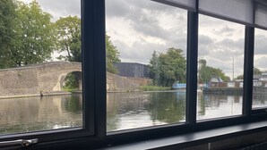 Vista attraverso una finestra di un canale con un ponte in mattoni e palazzi sullo sfondo.