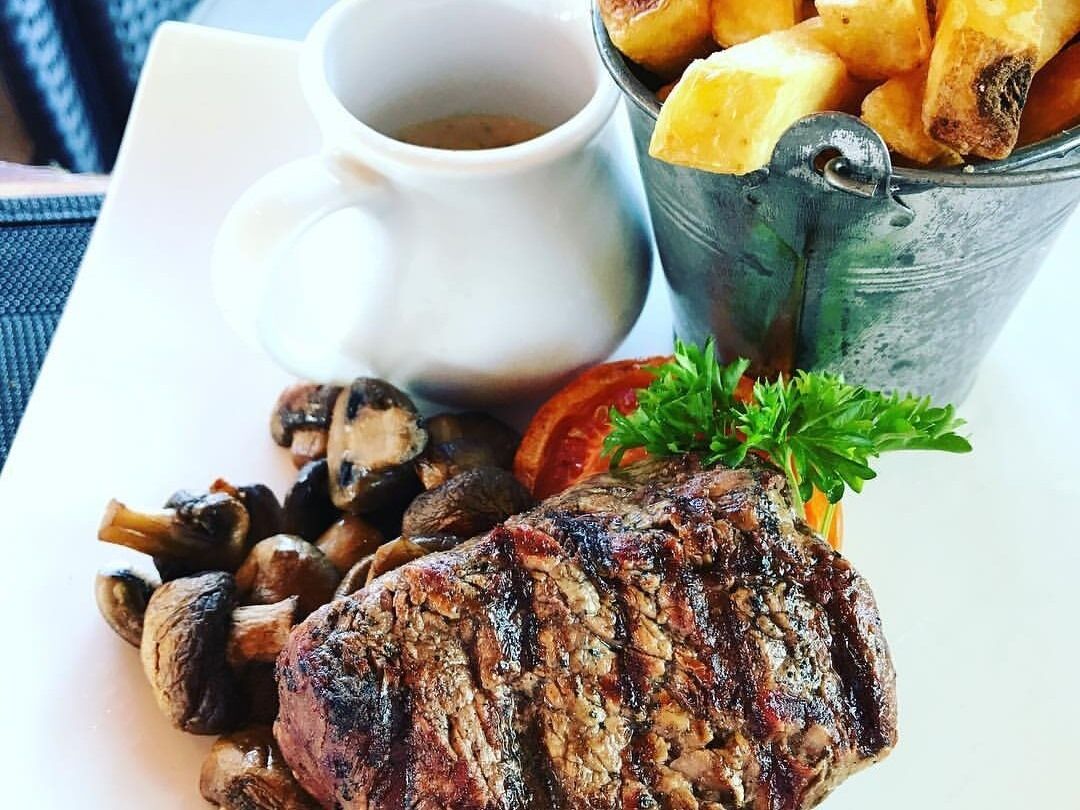 A plate with a grilled steak, mushrooms, and fries, accompanied by a cup of coffee.