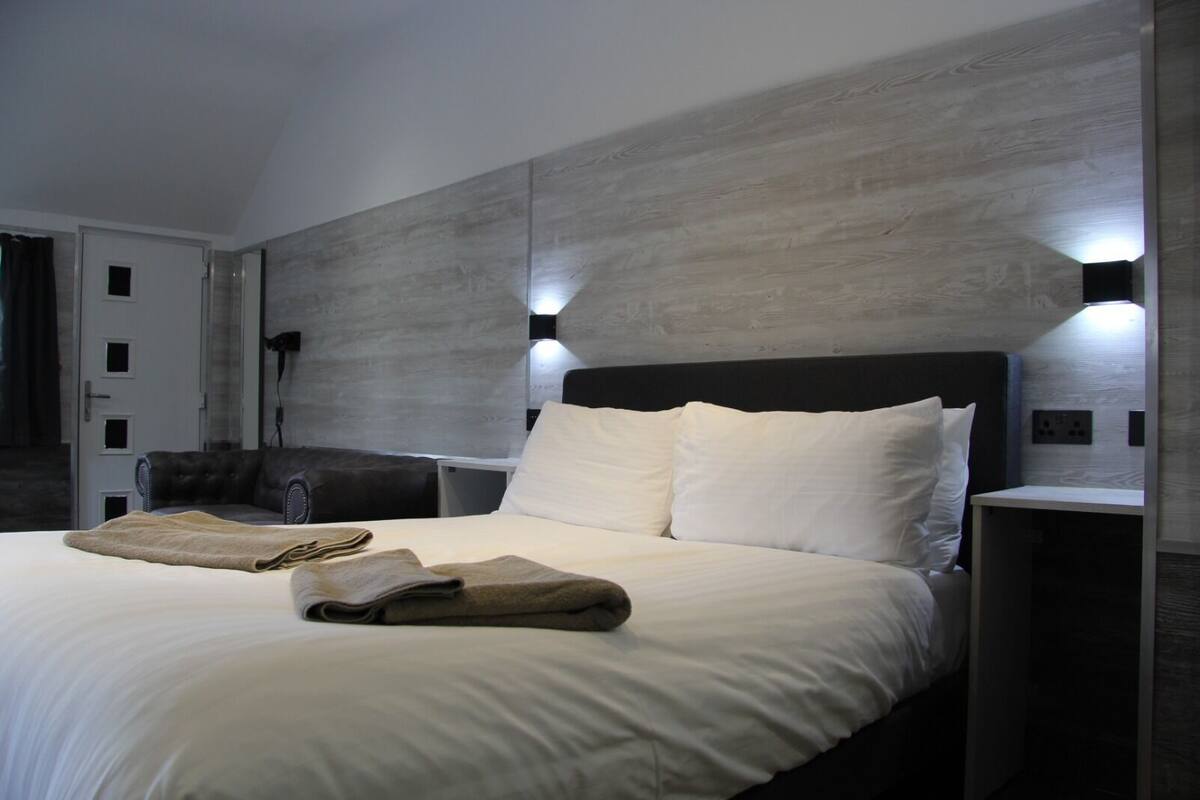 A modern hotel room with a large bed, a dark headboard, and two wall-mounted reading lights.