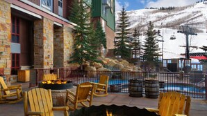 Un patio con sillas Adirondack, un brasero y un área de piscina con vistas a montañas nevadas y un telesilla al fondo.