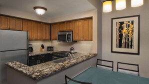 Una cocina moderna con encimeras de granito, electrodomésticos de acero inoxidable, armarios de madera y un comedor con mesa y sillas.