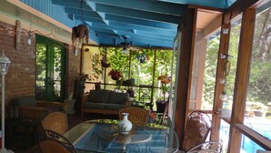 A covered patio area with a glass table, wicker chairs, a sofa, and potted plants.