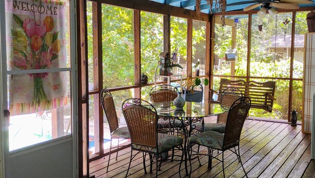 A covered patio with a glass door displaying a welcome sign, wicker chairs, a glass table, and a ceiling fan.