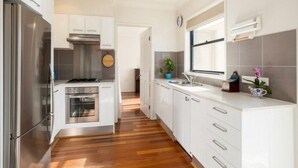 Une cuisine moderne avec des meubles blancs, des appareils en acier inoxydable, un plancher en bois et une fenêtre qui laisse entrer la lumière naturelle.