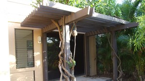 Un bâtiment doté d’une structure en forme de pergola, d’un chemin en pierre et d’un arbre recouvert de plantes grimpantes.