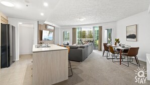 A modern apartment with a kitchen, dining area, and living room. It features a large window, a flat-screen TV, and a dining table with chairs.