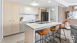 A modern kitchen with a central island, bar stools, and a large window with a cityscape view.