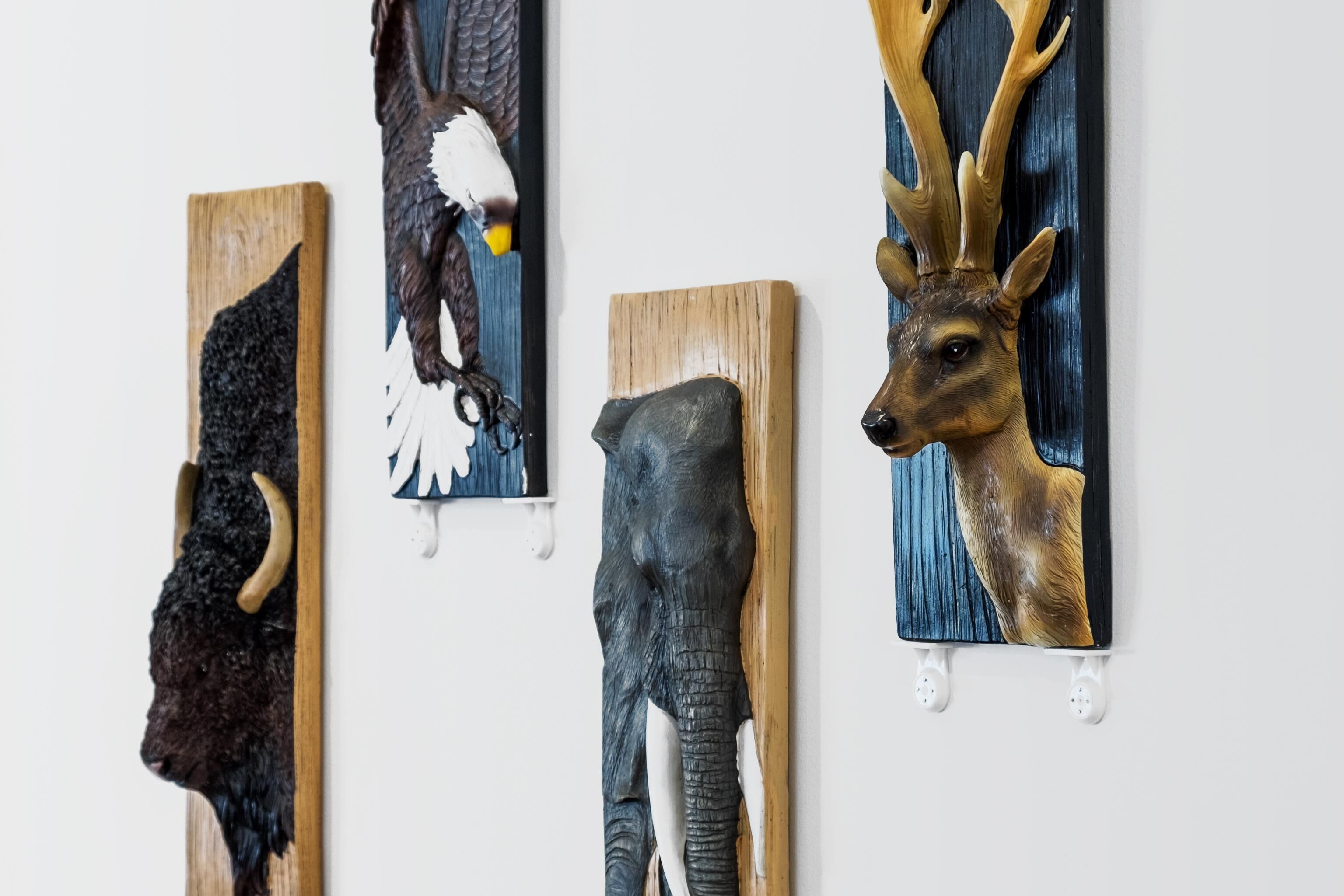 Vier an der Wand befestigte Tierkopfskulpturen.