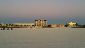 Una playa con una hilera de edificios, incluyendo un hotel alto y un edificio más pequeño con fachada dorada.