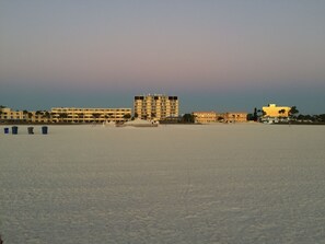 A beach with a row of buildings, including a tall hotel and a smaller building with a golden facade.