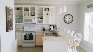 Une cuisine moderne avec des meubles blancs, un îlot central doté de sièges, un four à micro-ondes, un four traditionnel et une horloge murale.