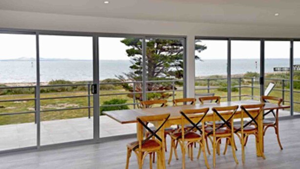 A dining area with a table and chairs, large windows with a view of the sea, and a modern architectural design.