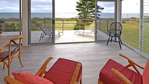 A spacious balcony with a view of the ocean, wooden chairs, and a dining table.