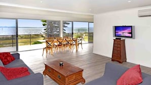A spacious living area with a large window overlooking a scenic view, a wooden coffee table, and a television on the wall.