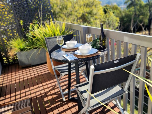 Une terrasse avec une table dressée pour deux personnes, agrémentée d’une bouteille de vin, de verres et de bols.