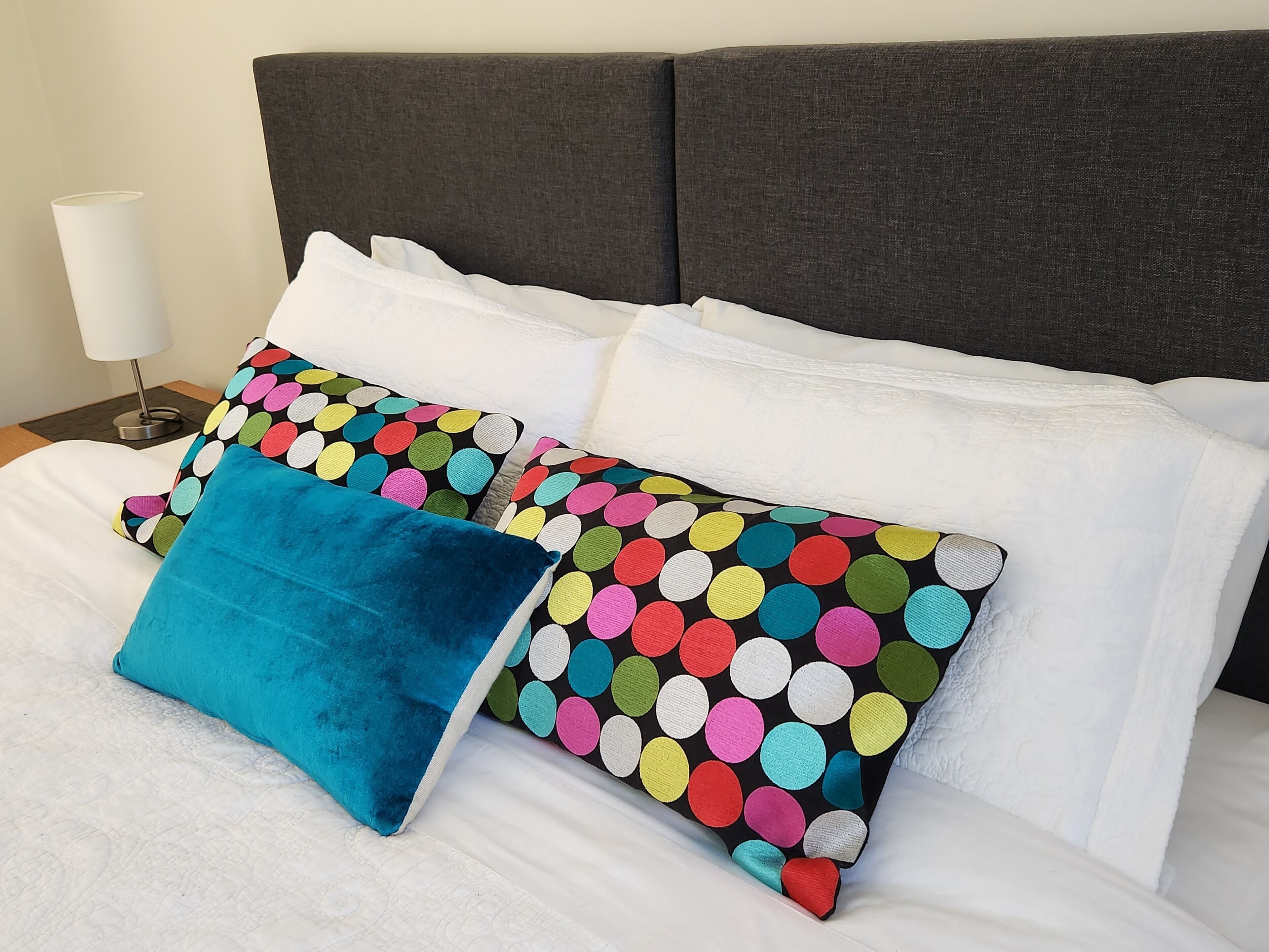 Ein Bett mit weißer Bettwäsche und mehreren Kissen, darunter eines blau und eines mit Punkten.