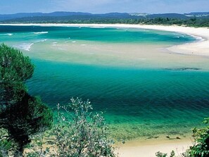 Un paysage côtier caractérisé par une eau turquoise cristalline, une plage de sable et une végétation luxuriante.