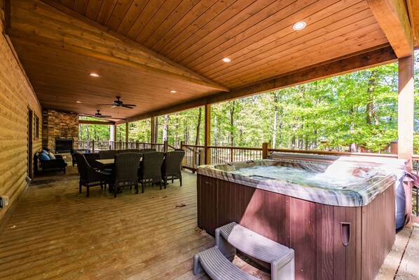 Una terraza de madera con un jacuzzi, mobiliario exterior y un muro de piedra.