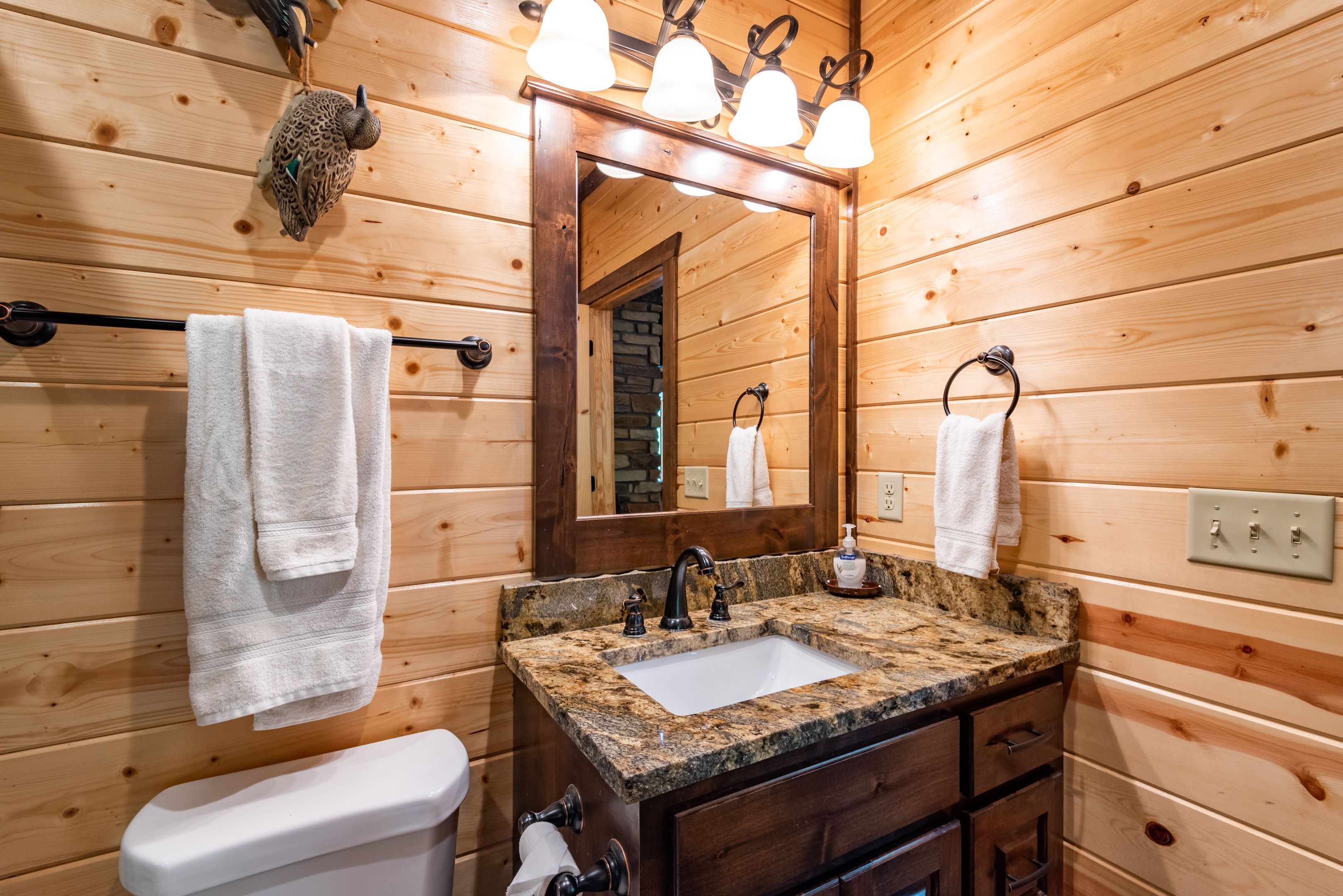 A wooden cabin bathroom with a granite countertop sink, wooden cabinets, and a large mirror.