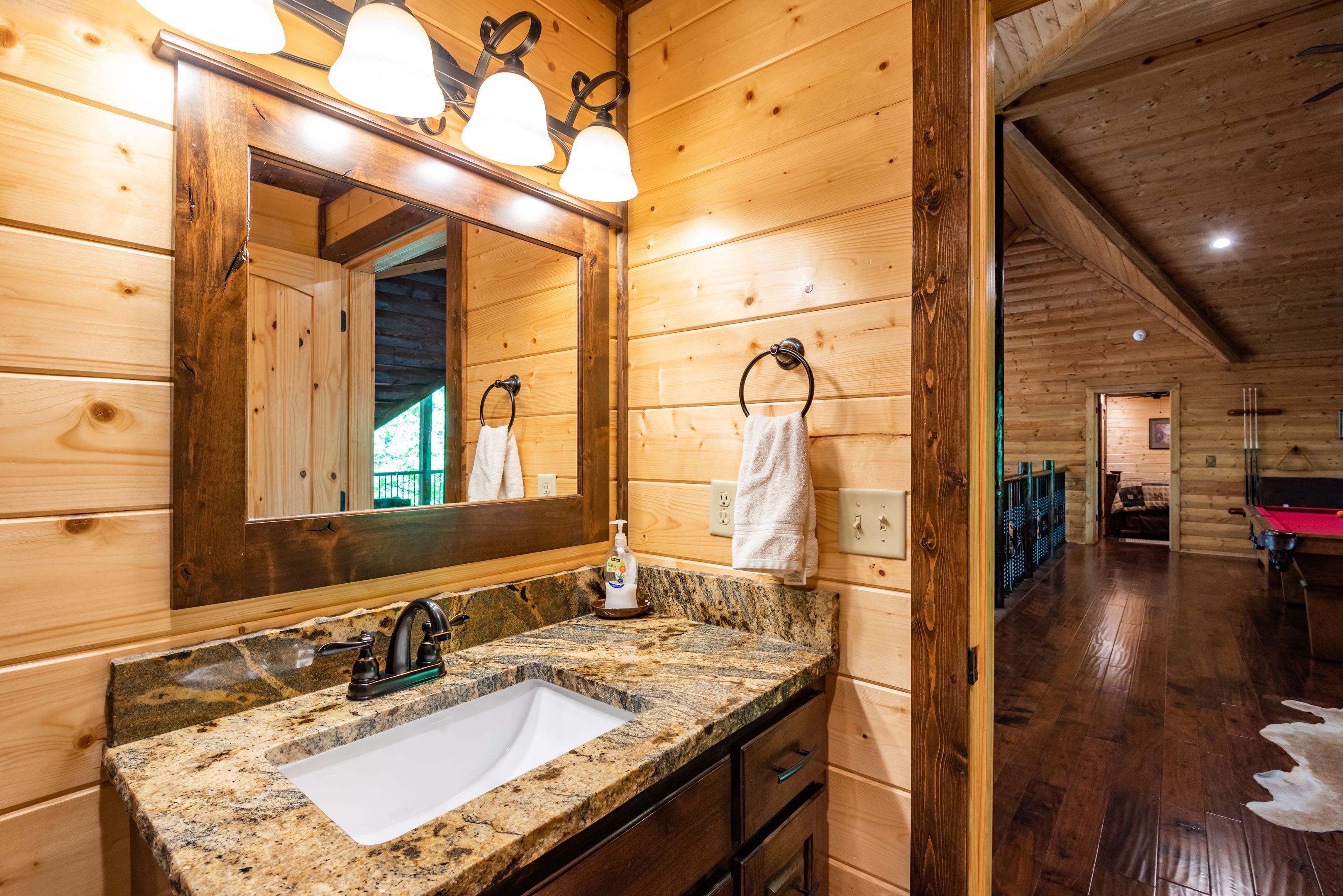 A wooden cabin interior with a granite sink, wooden walls, and a mirrored vanity.