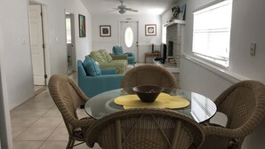 A dining area with wicker chairs and a glass table, a sofa with patterned cushions, a ceiling fan, and a brick fireplace. - Cottage with Pool and Dockage, just minutes to Key West (Cudjoe Key)