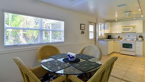 A dining area with a glass table and wicker chairs, a kitchen with white cabinets and appliances, and a window with blinds. - Cottage with Pool and Dockage, just minutes to Key West (Cudjoe Key)