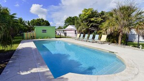 A swimming pool with a curved edge, surrounded by a concrete deck. There are lounge chairs and a small green structure nearby. - Cottage with Pool and Dockage, just minutes to Key West (Cudjoe Key)