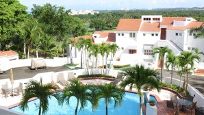 A pool area with palm trees, white buildings, and a view of distant buildings. - Rio Mar Beach Resort - Time Magazine TOP 100 World's Greatest Places  2018 (Rio Grande)