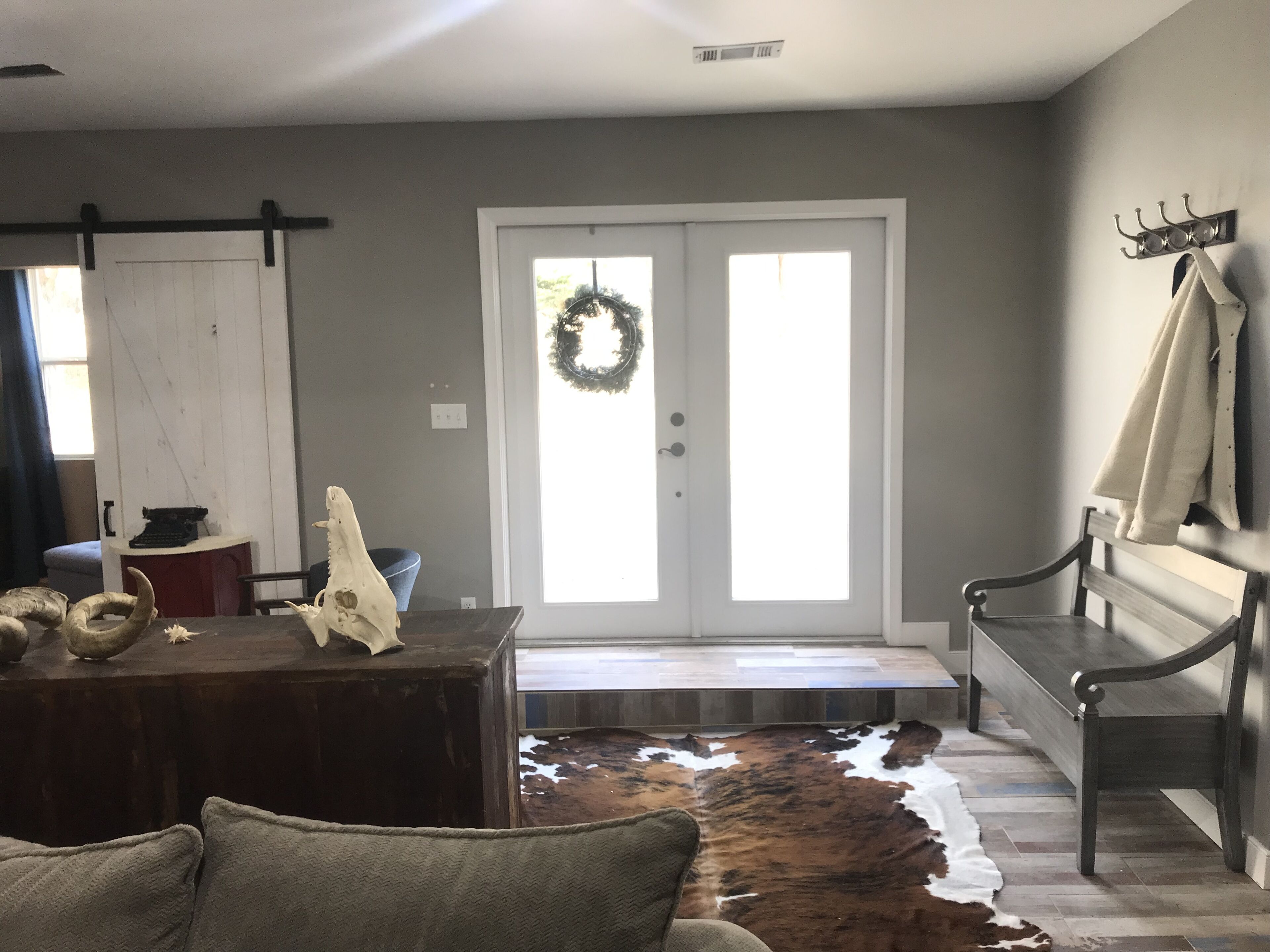 A room with a wooden bench, a cowhide rug, a desk with a typewriter, and a door with a wreath.
