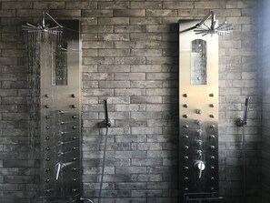 A modern shower with multiple heads against a brick wall.