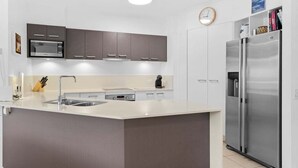 A modern kitchen with a central island, stainless steel appliances, and a clock on the wall. - Unit 2 'Point Break' (Point Arkwright)