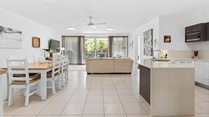 A modern kitchen with a central island, white cabinetry, and a dining area with a wooden table and chairs. - Unit 2 'Point Break' (Point Arkwright)