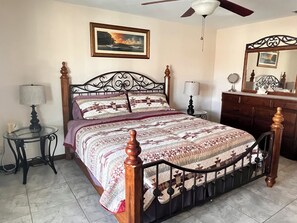 A bedroom with a bed, a ceiling fan, a dresser, a mirror, and a wall-mounted picture.