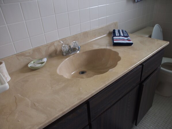 A bathroom with a beige sink, dark wooden cabinets, and a white tiled wall.