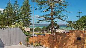 A coastal view with a brick wall, a large tree, and a beach in the background.