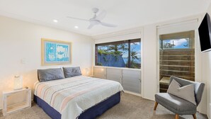 A bedroom with a bed, a chair, a ceiling fan, a window with a view, and a framed picture on the wall.