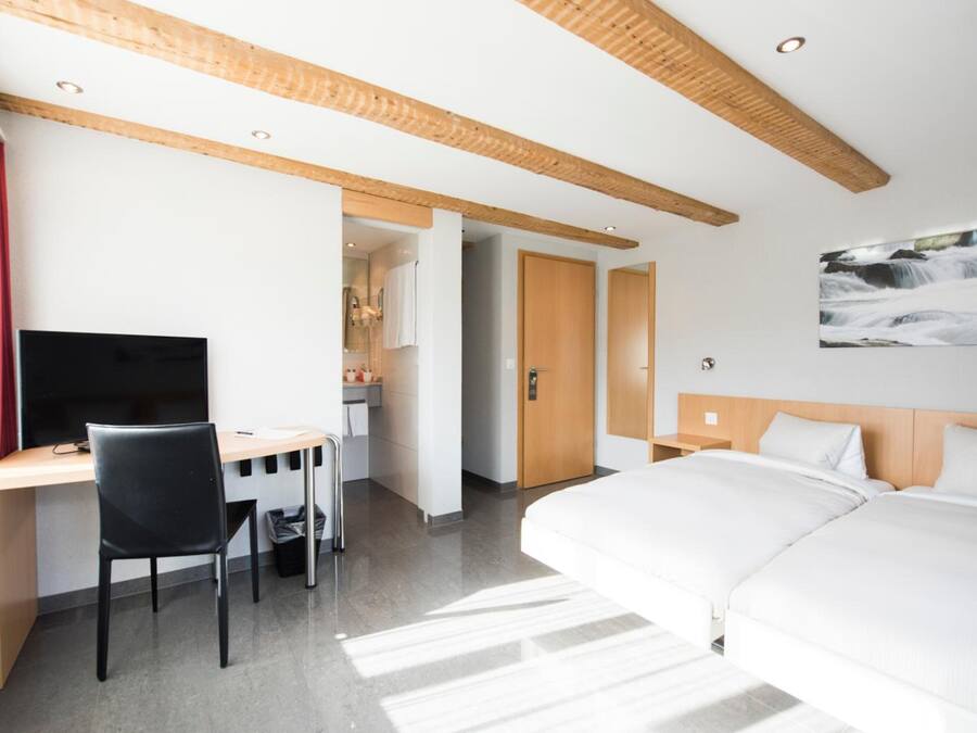A hotel room with a bed, a desk with a chair, a TV, and a painting on the wall.