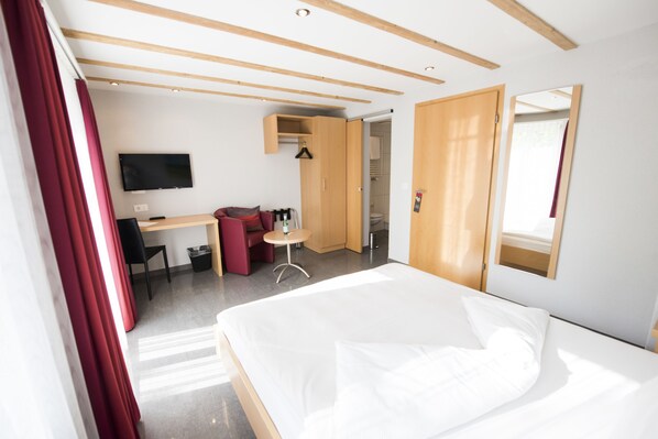 Quarto de hotel com cama, escrivaninha, cadeira, televisão e armário.