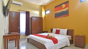 A hotel room with a bed, a desk, a nightstand, a TV, and a painting on the wall. - RedDoorz @ Uluwatu Bali (Pecatu)
