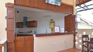 A kitchen with wooden cabinets, a tiled floor, and a small statue on the counter. - RedDoorz @ Uluwatu Bali (Pecatu)